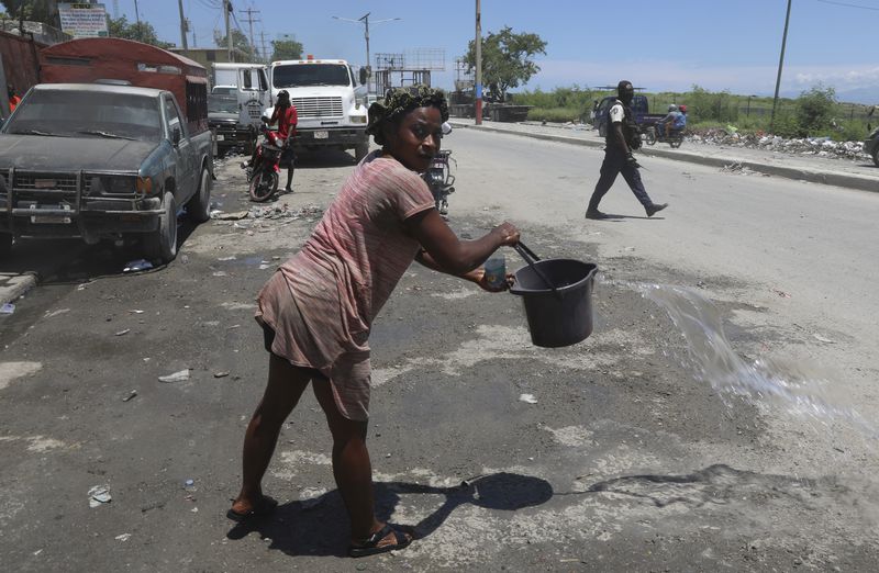 A woman empties a bucket of water on the street where police patrol near the airport in Port-au-Prince, Haiti, Friday, May 24, 2024. (AP Photo/Odelyn Joseph)