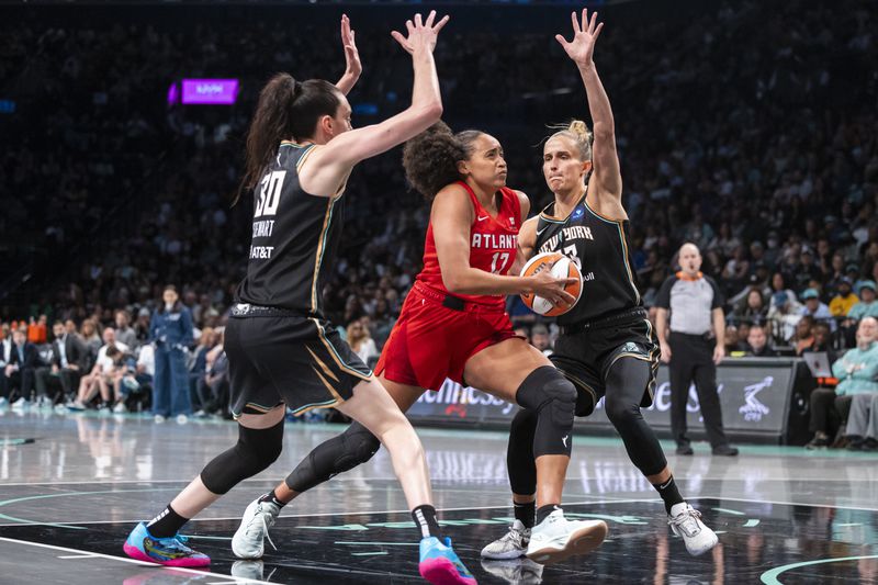 Atlanta Dream guard Haley Jones (13) drives between New York Liberty forwards Breanna Stewart (30) and Leonie Fiebich, front right, during the second half of a WNBA basketball first-round playoff game Sunday, Sept. 22, 2024, in New York. (AP Photo/Corey Sipkin)