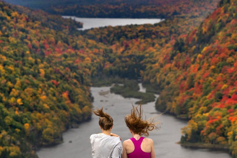 FILE - Wind whips the hair of two visitors taking in the view at the Indian Head vista overlooking Lower Ausable Lake in the Adirondacks, Sept. 27, 2020, near Keene Valley, N.Y. (AP Photo/Robert F. Bukaty, File)