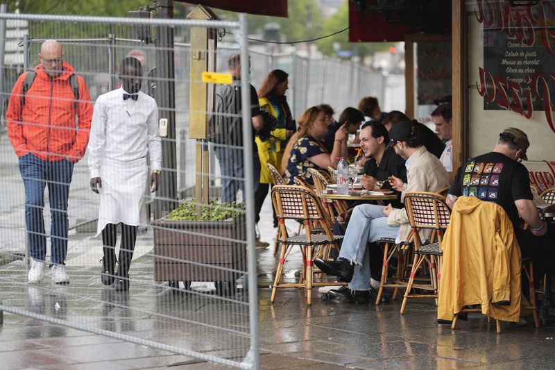 FILE - Patrons sit outside a restaurant behind some remaining security barriers on a street along the River Seine, now opened to foot traffic after Friday's opening ceremony at the 2024 Summer Olympics, July 27, 2024, in Paris, France. (AP Photo/Rebecca Blackwell, File)