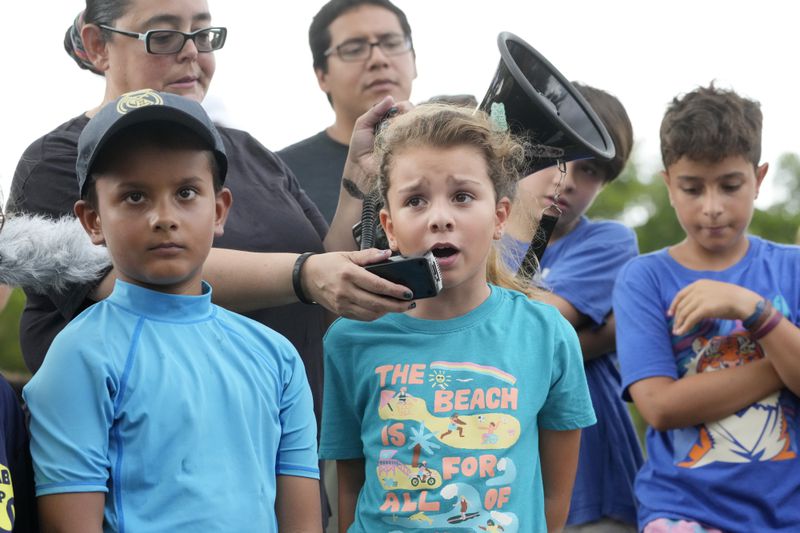 Helena Lourenco, center, 8, speaks out during a protest against Gov. Ron DeSantis' plan to develop state parks with business ventures such as golf courses, pickleball courts and large hotels, during a demonstration at Oleta River State Park, Tuesday, Aug. 27, 2024, in North Miami Beach, Fla. (AP Photo/Wilfredo Lee)