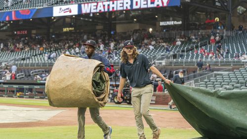 Ground crew workers remove tarps before a baseball game between the Cincinnati Reds and Atlanta Braves, Tuesday, July 23, 2024, in Atlanta. (AP Photo/Jason Allen)