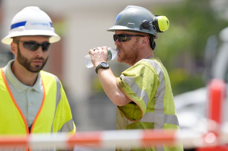 A worker, right, takes a drink of water while working in temperatures above 90F (32C) at a gas line work site, Thursday, June 20, 2024, on a street in Boston. (AP Photo/Steven Senne)