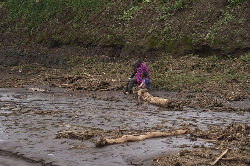 FILE - A man sits with children on a log, after floodwater washed away houses, in Kamuchiri Village Mai Mahiu, Nakuru County, Kenya, April 30, 2024. The impact of the calamitous rains that struck East Africa from March to May was intensified by a mix of climate change and rapid growth of urban areas, an international team of climate scientists said in a study. (AP Photo/Brian Inganga, File)