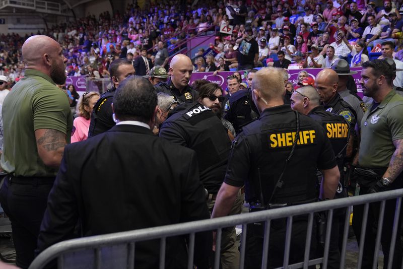 Police remove a man, center with sunglasses, who had climbed onto the media riser, as Republican presidential nominee former President Donald Trump speaks at a campaign event, Friday, Aug. 30, 2024, in Johnstown, Pa. (AP Photo/Alex Brandon)