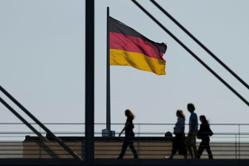 People walk in front of a German national flag on a bridge between parliament buildings in Berlin, Germany, Monday, Sept. 2, 2024. (AP Photo/Markus Schreiber)