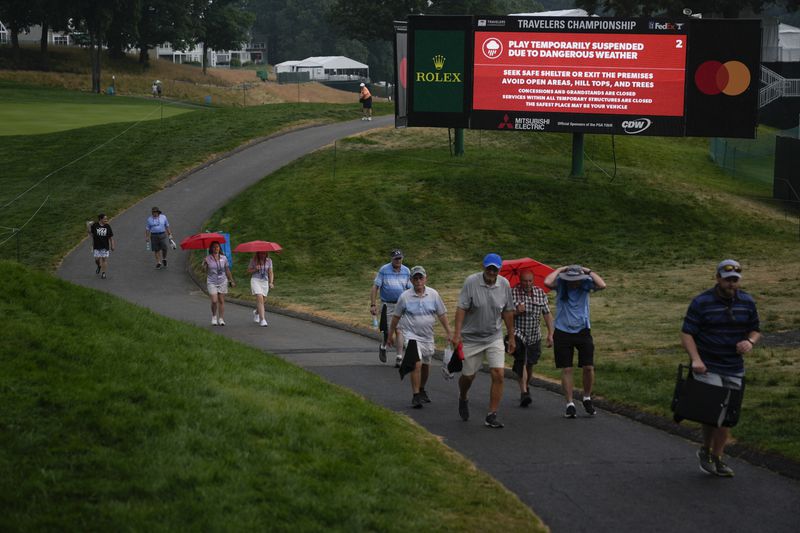 Fans walk past signs as play is suspended due to weather during the second round of the Travelers Championship golf tournament at TPC River Highlands, Friday, June 21, 2024, in Cromwell, Conn. (AP Photo/Seth Wenig)