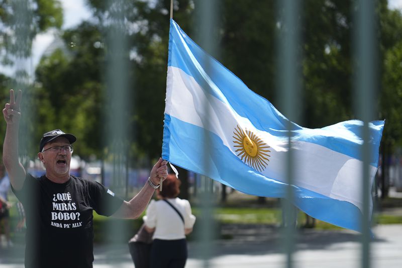 A demonstrators shows an Argentinian flag during a protest against the visit of Argentina's President Javier Milei for a meeting with German Chancellor Olaf Scholz in Berlin, Germany, Sunday, June 23, 2024. Banner reads: Milei for the hand, no to the base law. (AP Photo/Markus Schreiber)