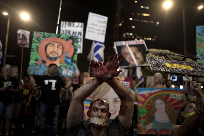 An activist wears theatrical blood, bound wrists and his mouth taped as relatives of hostages held by Hamas militants in the Gaza Strip and their supporters call for their immediate release and to protest against Israeli Prime Minister Benjamin Netanyahu's government in Tel Aviv, Israel, Saturday, Aug. 24, 2024. (AP Photo/Maya Alleruzzo)