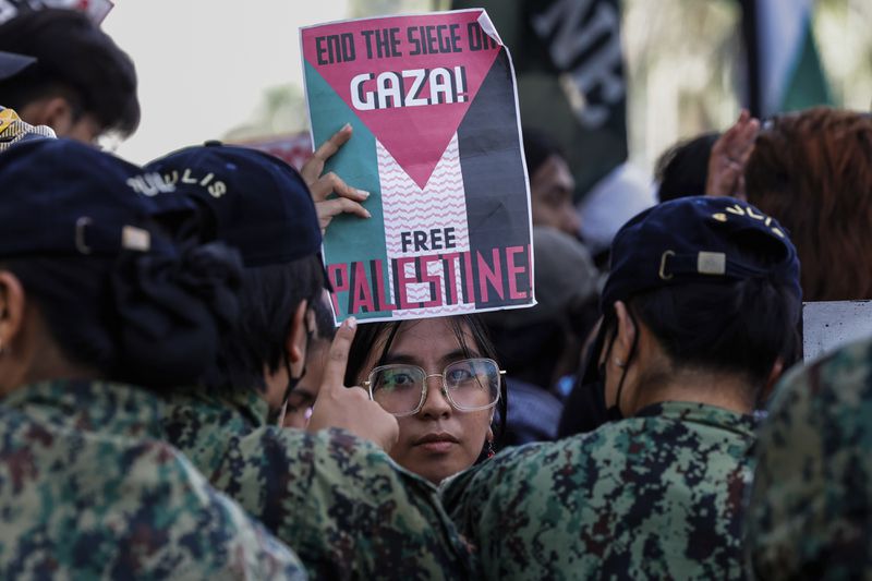 An activist raises a placard as police personnel block activists from marching near the U.S. Embassy in Manila on Saturday, Oct.5, 2024, as they hold a protest to observe the first-year anniversary of the war in Gaza.(AP Photo/Gerard V. Carreon)