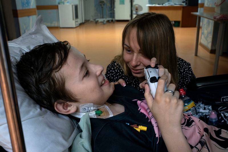 Yuliia Vasylenko smiles with her son Denys, 11, as he plays on a video game console at the National Cancer Institute in Kyiv, Ukraine, Wednesday, July 10, 2024. Denys is one of 31 young patients battling cancer who were relocated to the hospital from Okhmatdyt Children’s Hospital after it was struck by a Russian missile this week. (AP Photo/Alex Babenko)