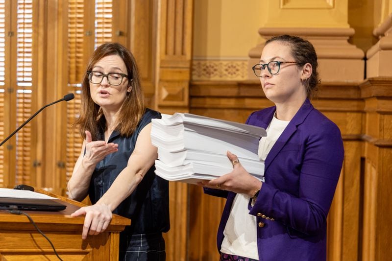 Kristin Nabers, state director for All Voting is Local Action, makes public comment against new proposed rules during a Georgia Election Board meeting at the Capitol in Atlanta on Friday, September 20, 2024, as colleague Marissa Pyle holds a 1872 pieces of paper to demonstrate what a stack of ballots might look like. (Arvin Temkar / AJC)