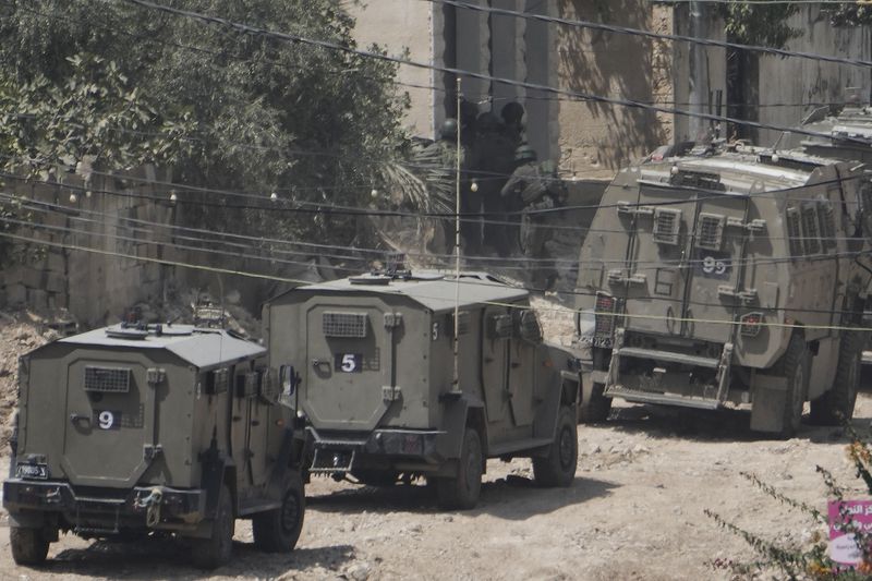 Member of the Israeli forces take position next to the armoured vehicles during a military operation in the West Bank Jenin refugee camp, Saturday, Aug. 31, 2024. (AP Photo/Majdi Mohammed)