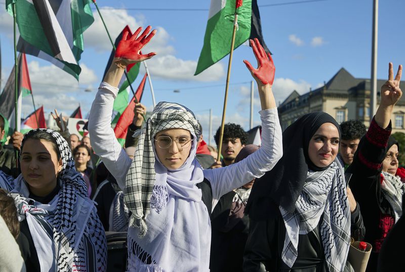 A participant in a pro-Palestinian rally holds up her red-painted hands on the Steintordamm, in Hamburg, Germany, Saturday, Oct. 5, 2024. (Georg Wendt/dpa via AP)