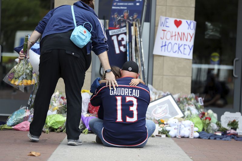 Hylas Stemen, sitting, of Columbus, mourns at a memorial set up by fans for Blue Jackets hockey player Johnny Gaudreau in Columbus, Ohio, Aug. 30, 2024. Gaudreau, along with his brother Matthew, was fatally struck by a motorist while riding his bicycle on Thursday. (AP Photo/Joe Maiorana)