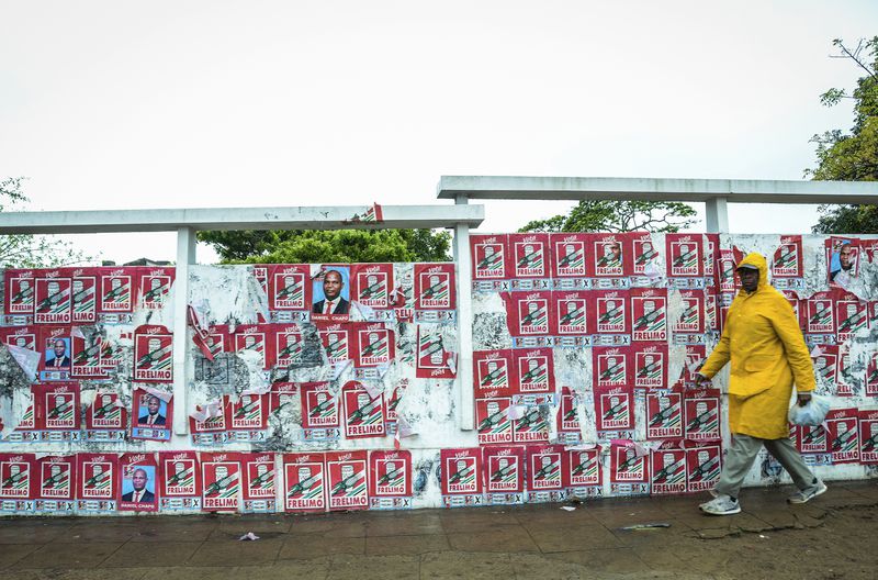 A pedestrian passes a wall of election posters in Maputo, Sunday, Oct. 6, 2024, ahead of elections to be held in Mozambique. (AP Photo/Carlos Uqueio)