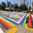 A runner crosses the rainbow crosswalk in Midtown Atlanta on Monday, Oct. 7, 2024. The crosswalk got an inclusive makeover with black and brown stripes to represent communities of color and to showcase the colors of the transgender flag. (Arvin Temkar / AJC)