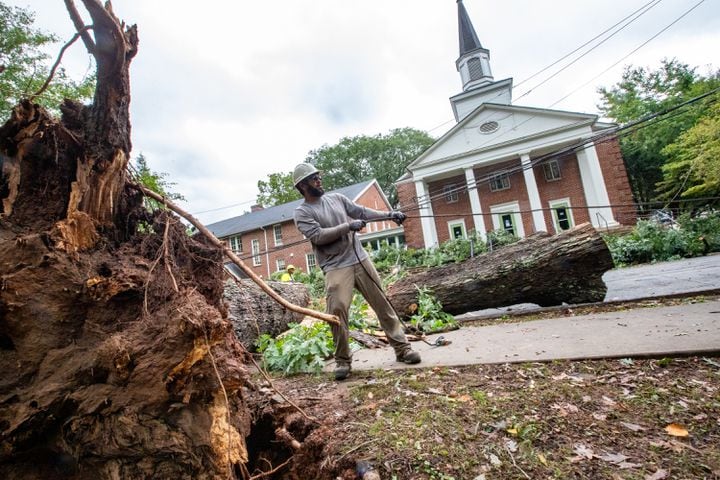 Damage from hurricane Helene along McClendon Ave in Candler Park blocks the road in front of Neighborhood Church and pulled down power lines along the road.  Agustin Gomez, who works for Garrison Tree Inc., works a wench after moving a large oak tree out of the road on Friday, Sept 27, 2024.  (Jenni Girtman for The Atlanta Journal-Constitution)