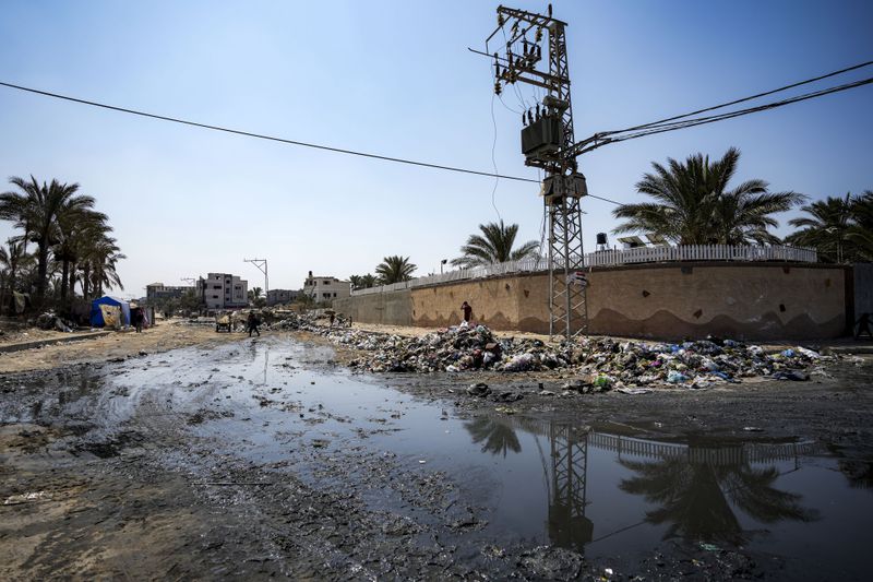 Palestinians displaced by the Israeli air and ground offensive on the Gaza Strip walk next a dark streak of sewage flowing into the streets of Deir al-Balah, central Gaza Strip, Tuesday, Aug. 27, 2024. (AP Photo/Abdel Kareem Hana)