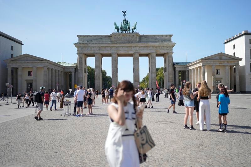 People stand in front of Berlin's famous landmark 'Brandenburg Gate' in Berlin, Germany, Monday, Sept. 2, 2024. (AP Photo/Markus Schreiber)