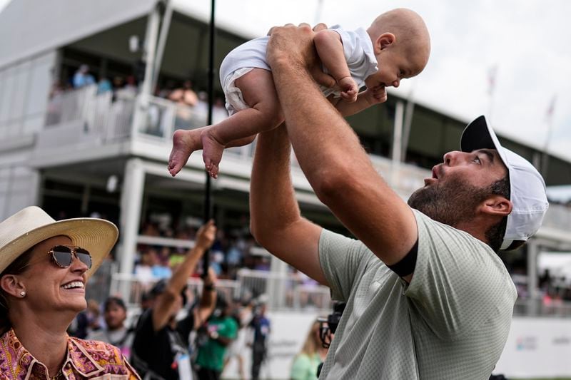 Scottie Scheffler holds his son Bennett Ezra Scheffler as his wife Meredith Scudder looks on on the 18th green after Scheffler won the final round of the Tour Championship golf tournament, Sunday, Sept. 1, 2024, in Atlanta. (AP Photo/Mike Stewart)