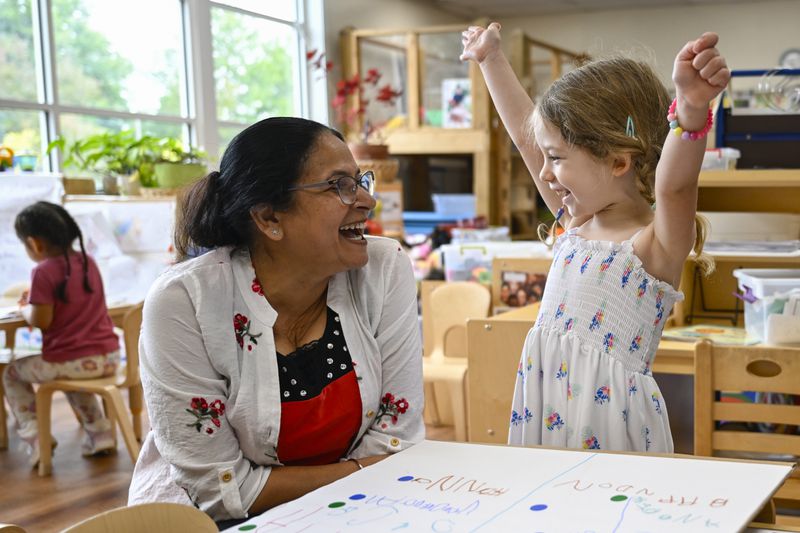 Preschool teacher Jasmeet Kaur, left, watches the reaction of her student Naomi when she discovers that her favorite character of the TV show PAW Patrol won the class vote for the room's favorite character of the show at the ACCA Child Development Center, Thursday, Sept. 19, 2024, in Annandale, Va. The students are getting foundational lessons on how to live in a democracy by allowing them to regularly vote on different things through out the day. (AP Photo/John McDonnell)