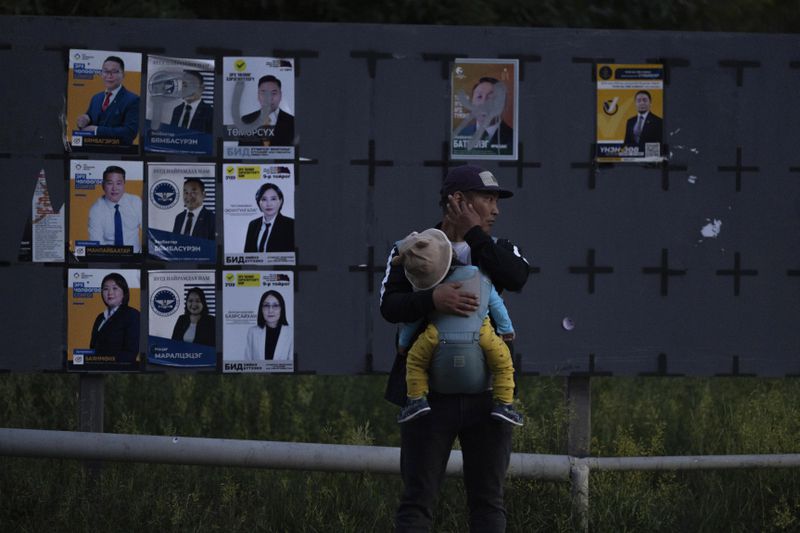 FILE - A man carries a child near candidates' posters two days before polls open in Ulaanbaatar, Mongolia, Wednesday, June 26, 2024. A parliamentary election will be held in Mongolia on Friday, June 28, 2024 for the first time since the body was expanded to 126 seats, adding some uncertainty to a system that has been monopolized by two political parties and plagued by corruption. (AP Photo/Ng Han Guan, File)
