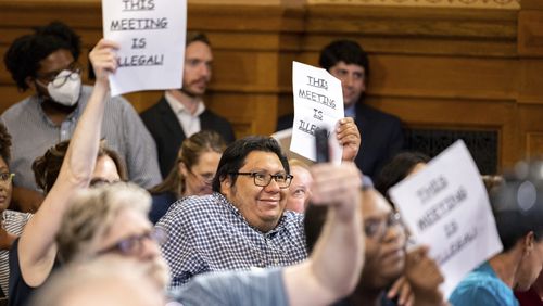 Attendees hold signs that say "This Meeting is Illegal" during a hastily planned State Election Board meeting at the Capitol in Atlanta last  Friday. (Arvin Temkar/Atlanta Journal-Constitution via AP)