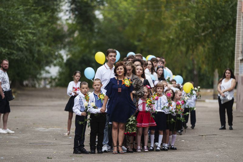 First-grades wait with a teacher for the start of the traditional ceremony for the first day of school in Zaporizhzhia, Ukraine, Sunday Sept. 1, 2024. Zaporizhzhia schoolchildren celebrated the traditional first day of school near the frontline. With the front just 40 kilometers away, the war is never far from the minds of teachers and families. (AP Photo/Evgeniy Maloletka)