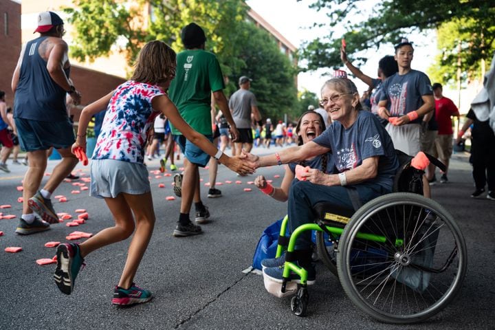 Dixie, a patient at the Shepherd Center, high-fives a passing runner during the 55th running of The Atlanta Journal-Constitution Peachtree Road Race at "Cardiac Hill" on Peachtree Road NW in Atlanta on Thursday, July 4, 2024. (Seeger Gray / AJC)