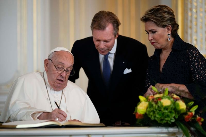 Pope Francis flanked by Luxembourg's Grand Duke Henri and Grand Duchess Maria Teresa signs the guest book during his visit at the Grand Ducal Palace, in Luxembourg, Thursday, Sept. 26, 2024. (AP Photo/Andrew Medichini)