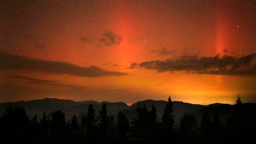 Flares of northern lights color the sky over the White Mountains just after midnight, Friday, Sept. 13, 2024, as viewed from mountaintop in Chatham, N.H. Lights on the summit of Mount Washington can be seen on the ridgeline at left. (AP Photo/Robert F. Bukaty)