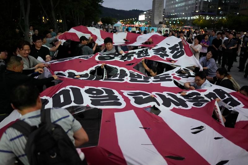 Protesters tear a huge banner as they oppose the meeting between South Korean President Yoon Suk Yeol and Japanese Prime Minister Fumio Kishida in Seoul, South Korea, Friday, Sept. 6, 2024. The part of banner reads "South Korea-U.S.-Japan military alliance." (AP Photo/Lee Jin-man)