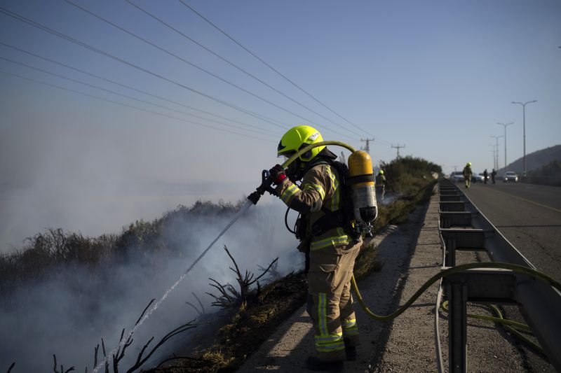 A firefighter works to extinguish a fire after a rocket, fired from Lebanon, hit an area next to a road near Kiryat Shmona, northern Israel, Saturday, Oct. 5, 2024. (AP Photo/Leo Correa)