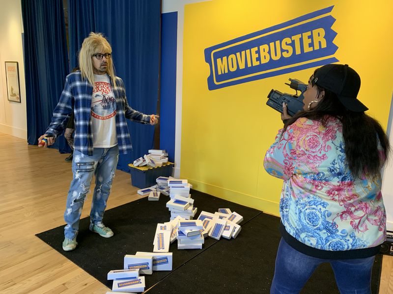 Actors Ace Marrero (left) and KymBerli Dee participate in the "Save the Video Store" interactive experience at The Avenue West Cobb May 14, 2022, loosely playing Garth and Wayne from "Wayne's World." RODNEY HO/rho@ajc.com