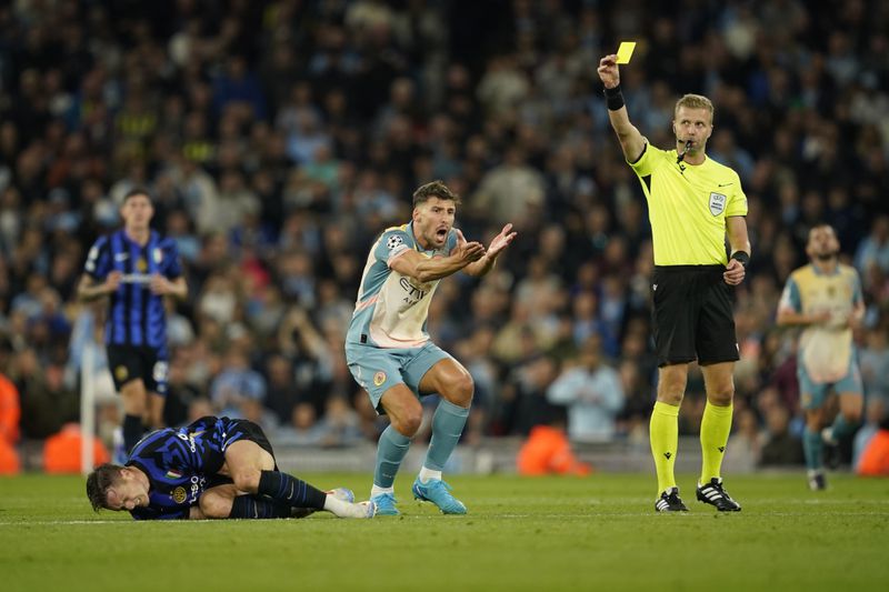 Manchester City's Ruben Dias, center, reacts as referee Glenn Nyberg, right, shows him a yellow card after he fouled Inter Milan's Piotr Zielinski, left, during the Champions League opening phase soccer match between Manchester City and Inter Milan at the Etihad Stadium, in Manchester, England, Wednesday, Sept. 18, 2024. (AP Photo/Dave Thompson)