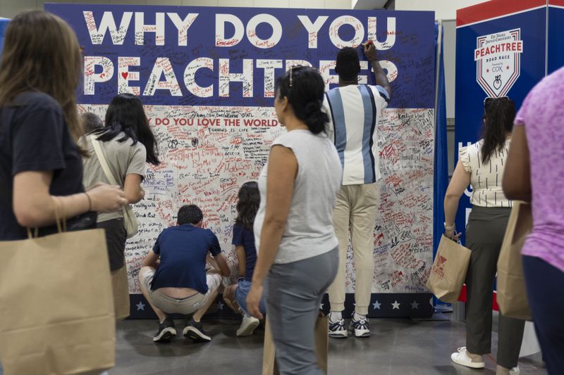 People write on a “Why do you Peachtree” board after picking up their bibs for the Atlanta Journal-Constitution Peachtree Road Race at the Peachtree Health and Fitness Expo in Atlanta on Tuesday, July 2, 2024.   (Ben Gray / Ben@BenGray.com)