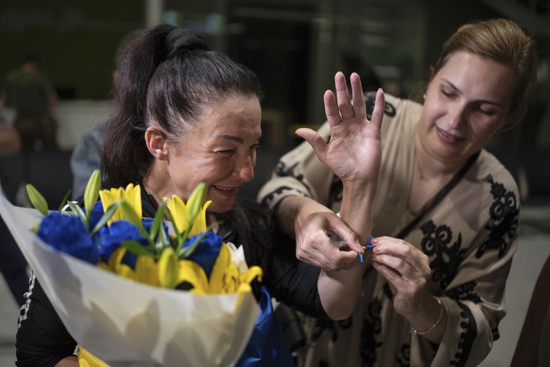 Olena Pekh, left, researcher at Horlivka Art Museum shows the bracelet on her arm while she speaks to her daughter via videosignal, in Kyiv airport, Ukraine, Saturday, June 29, 2024. Ten Ukrainians who had been held prisoners for years, were released from Russian captivity on Friday with a mediation of Vatican, said Ukraine's President Volodymyr Zelenskyy. (AP Photo/Alex Babenko)