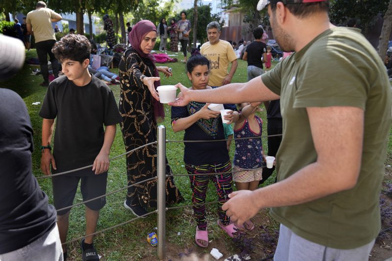 A man, right, distributes food for people who fled the southern suburb of Beirut amid ongoing Israeli airstrikes, at a park in downtown Beirut, Lebanon, Saturday, Sept. 28, 2024. (AP Photo/Hussein Malla)