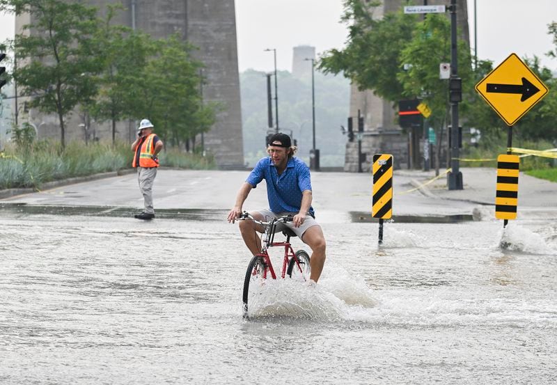 A person bikes across a flooded street due to a water main break in Montreal, Friday, Aug. 16, 2024, causing flooding in several streets of the area. (Graham Hughes/The Canadian Press via AP)