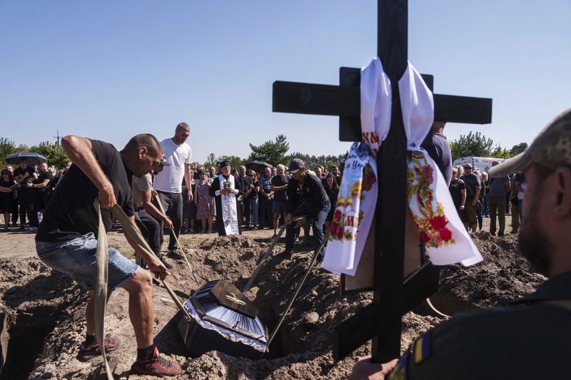 Funeral workers down a coffin into a grave during the funeral ceremony of six Ukrainian servicemen killed in a Russian rocket attack at a Ukrainian military academy, during their funeral ceremony in Poltava, Ukraine, Saturday Sept. 7, 2024. (AP Photo/Evgeniy Maloletka)