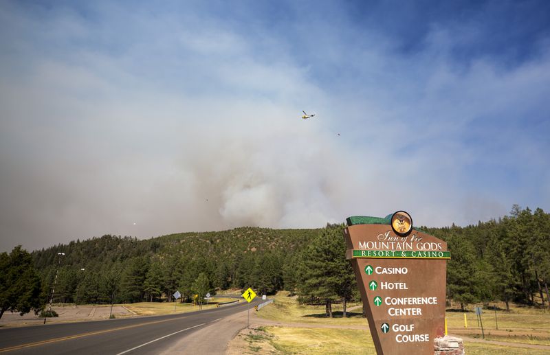 A helicopter flies over smoke from a wildfire seen from the Inn of the Mountain Gods Resort in Ruidoso, N.M., Tuesday, June 18, 2024. Thousands of residents fled their homes as a wildfire swept into the mountain village of Ruidoso in southern New Mexico. (AP Photo/Andres Leighton)