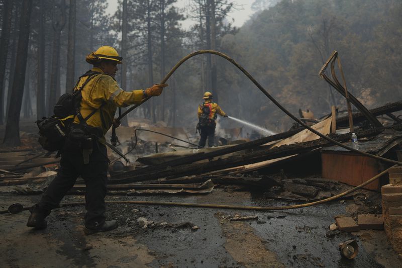 Firefighters hose down hot spots on a fire-ravaged property while battling the Bridge Fire Wednesday, Sept. 11, 2024, in Wrightwood, Calif. (AP Photo/Eric Thayer)