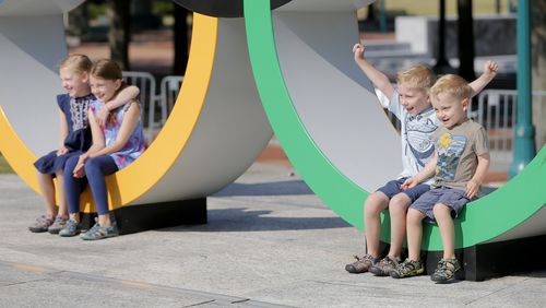 Calvan Parks, 6, raises his hand in the air while shouting, “Olympics,” as he poses for a photo with his siblings, from left to right, Amelia Parks, 11, Catherine Parks, 9, and Graham Parks, 3, at Centennial Olympic Park on Tuesday, July 27, 2021. Today marks 25 years since the bombing at the park during the Centennial Olympics in Atlanta. Convicted bomber Eric Robert Rudolph used a hidden bomb in his backpack to target the park. One person was killed, and over 100 people were injured. (Christine Tannous / christine.tannous@ajc.com)