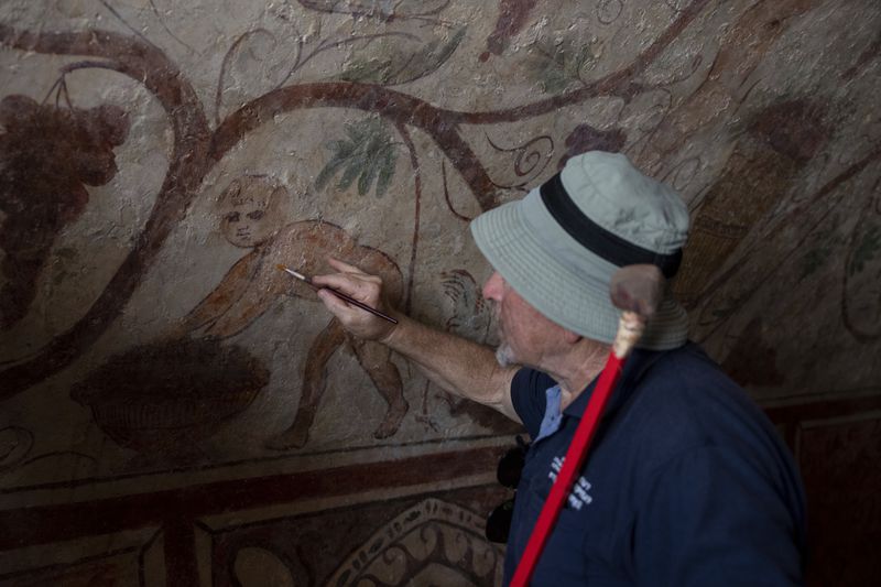 A worker points to an ancient wall of the archeological tomb site in Ashkelon, Israel, Tuesday, Aug. 27, 2024. The tomb with wall paintings depicting Greek mythological figures is at least 1,700 years old said the Israeli Antiquities Authority, whose workers are restoring the site. (AP Photo/Ohad Zwigenberg)