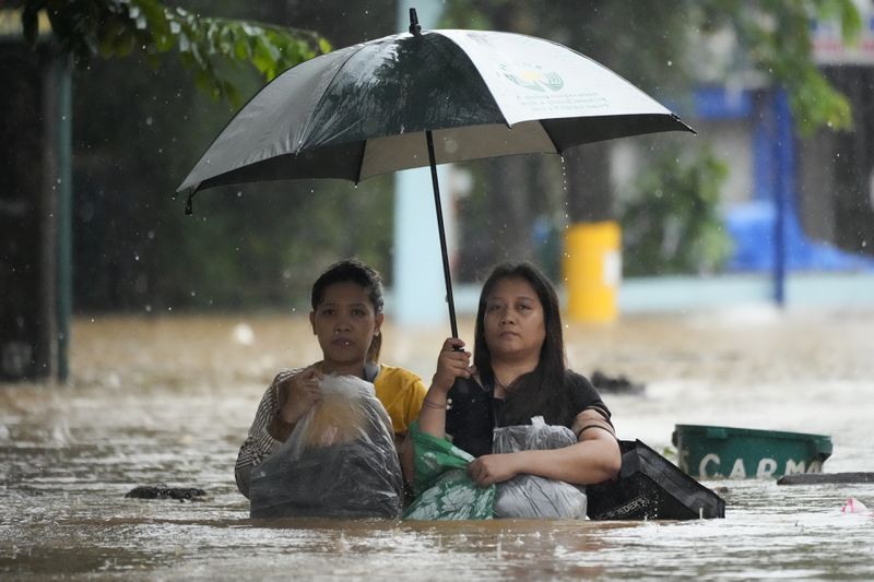 Residents protect their belongings as they negotiate a flooded street caused by heavy rains from Tropical Storm Yagi, locally called Enteng, in Cainta, Rizal province, Philippines, Monday, Sept. 2, 2024. (AP Photo/Aaron Favila)