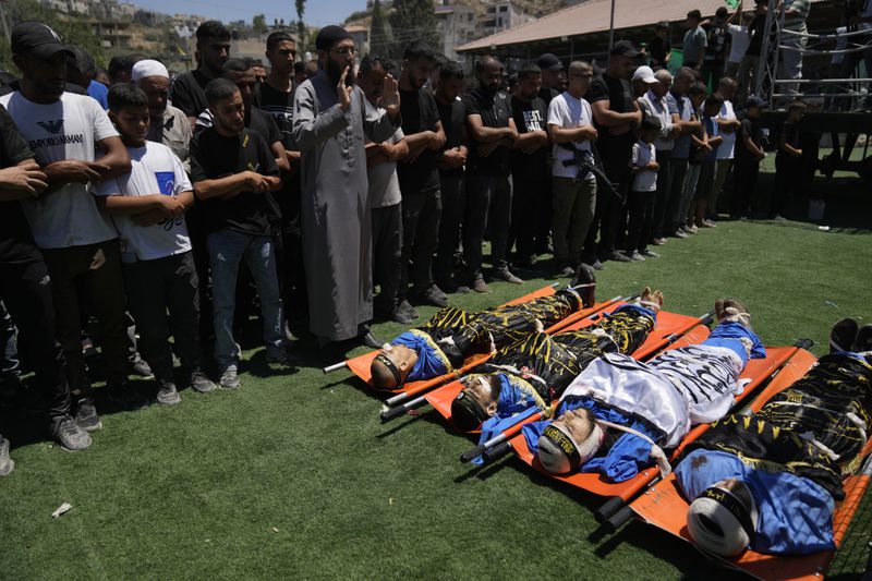 Mourners pray over the bodies wrapped with Islamic Jihad flags, of four Palestinians who were killed by an Israeli airstrike late Tuesday, during their funeral in the West Bank refugee camp of Nur Shams, near Tulkarem, Wednesday, July 3, 2024. Palestinian health officials say four Palestinians were killed by an Israeli airstrike in a refugee camp in the northern West Bank late Tuesday. Israel's military said an aircraft struck a group of militants who were planting explosives in Nur Shams refugee camp near Tulkarem. (AP Photo/Nasser Nasser)