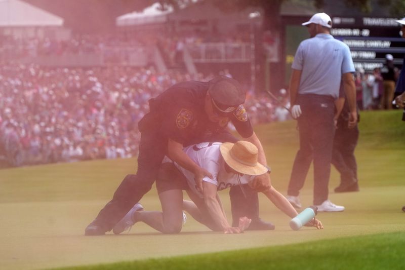 A protester is taken into custody after he ran onto the course as Scottie Scheffler, right, walks away on the 18th hole during the final round of the Travelers Championship golf tournament at TPC River Highlands, Sunday, June 23, 2024, in Cromwell, Conn. (AP Photo/Seth Wenig)