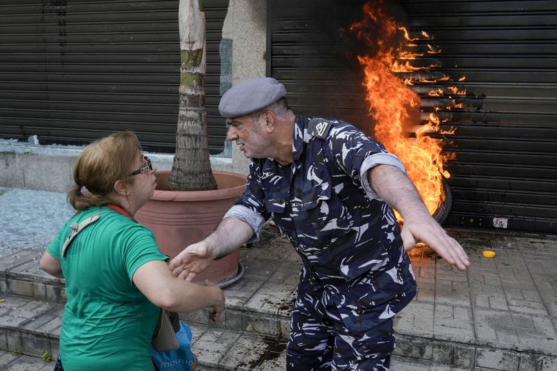 FILE - A police officer speaks with a protesting depositor as they stand in front of burning tires set on fire in front of a branch of Emirates Lebanese Bank in Dawra, a suburb north-east of Beirut, on Aug. 29, 2024. (AP Photo/Bilal Hussein, File)