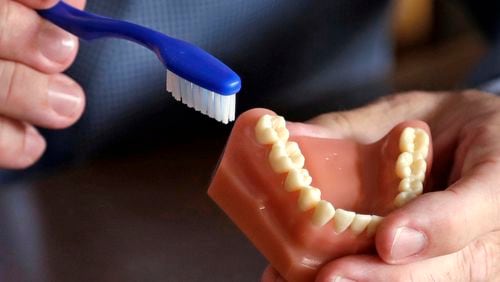 FILE - A dentist holds a model of teeth and a toothbrush in Seattle on Aug. 3, 2018. (AP Photo/Elaine Thompson, File)